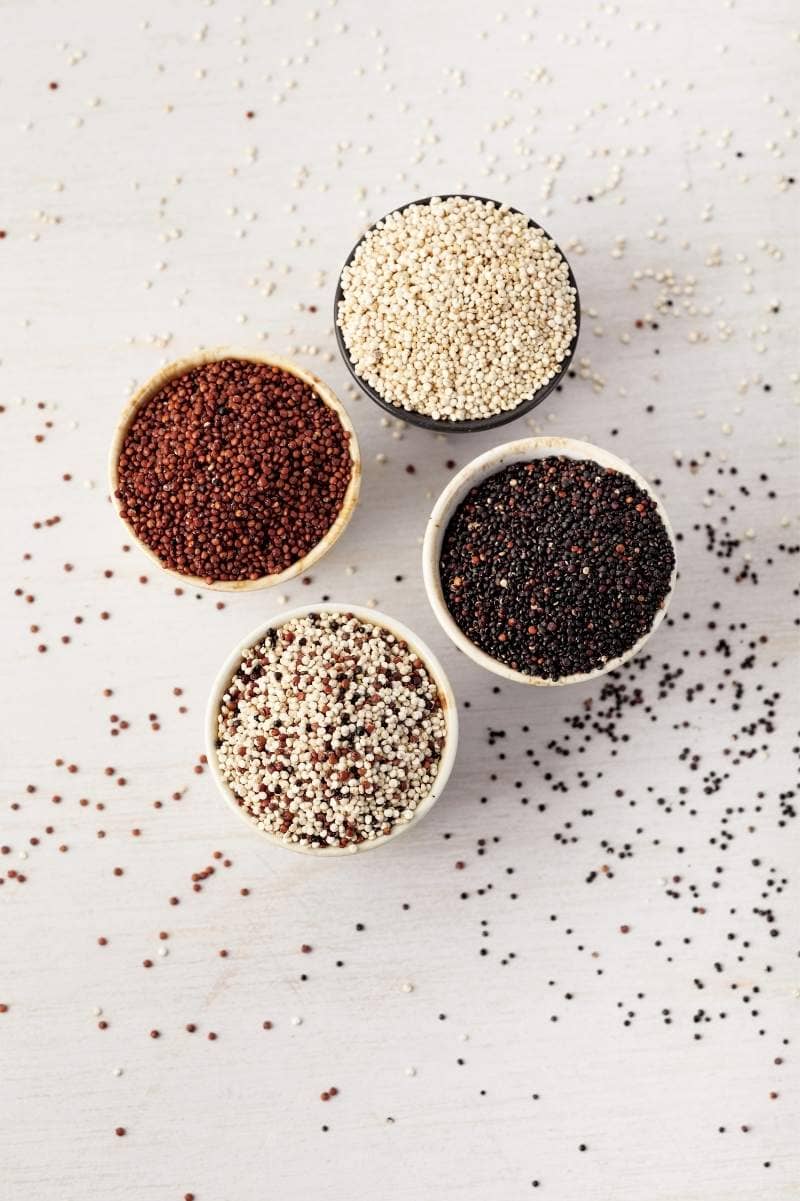 Four different varieties of quinoa in bowls such as red quinoa, black quinoa, and white quinoa.