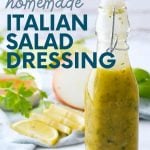 A glass flip-top bottle filled with homemade italian salad dressing sits on a counter in front of fresh ingredients. A text overlay reads, "Easy. Healthy. Cheap. Homemade Italian Salad Dressing."