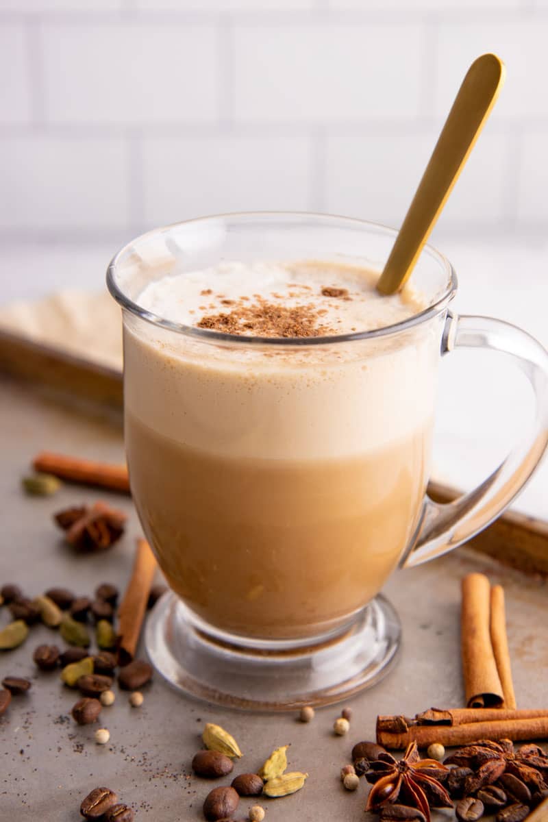 Dirty chai in a glass mug with whole spices around it such as cinnamon and cardamom.
