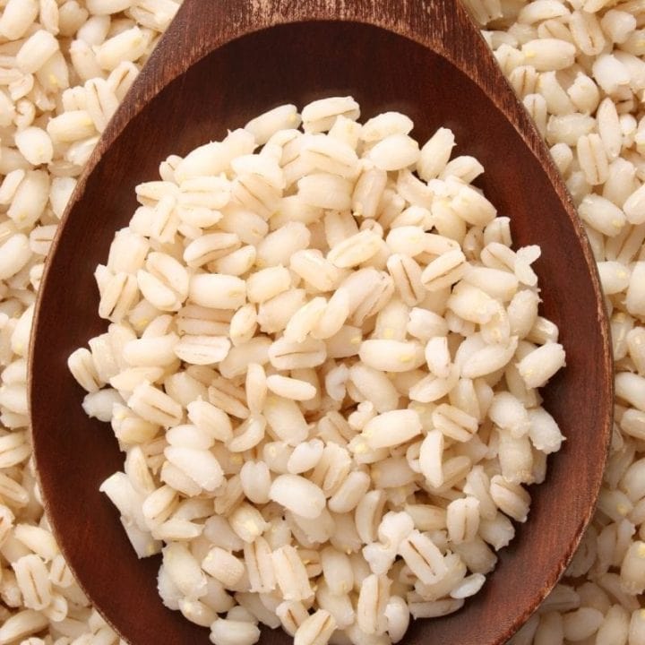 Close view of grains of barley on a wooden spoon.