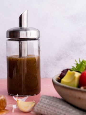 A glass cruet filled with balsamic vinaigrette stands beside a salad bowl filled with fresh ingredients.