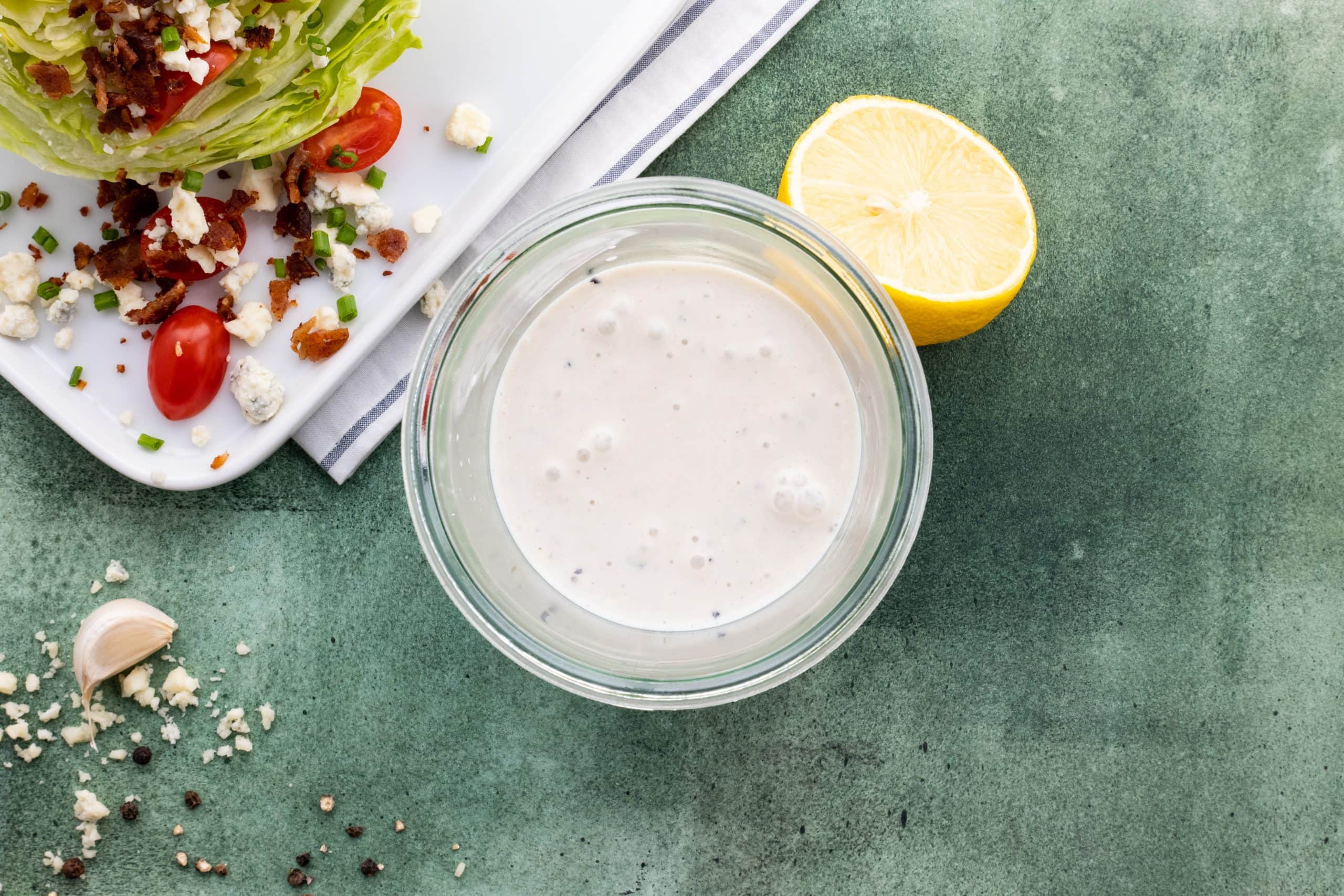 Top view of a glass jar filled with homemade dressing beside a plated wedge salad.