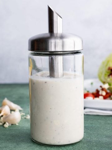Homemade blue cheese dressing in a cruet in front of a wedge salad.