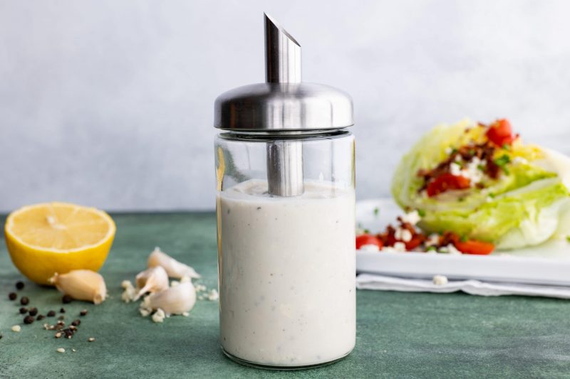 Homemade blue cheese dressing in a cruet in front of a wedge salad.