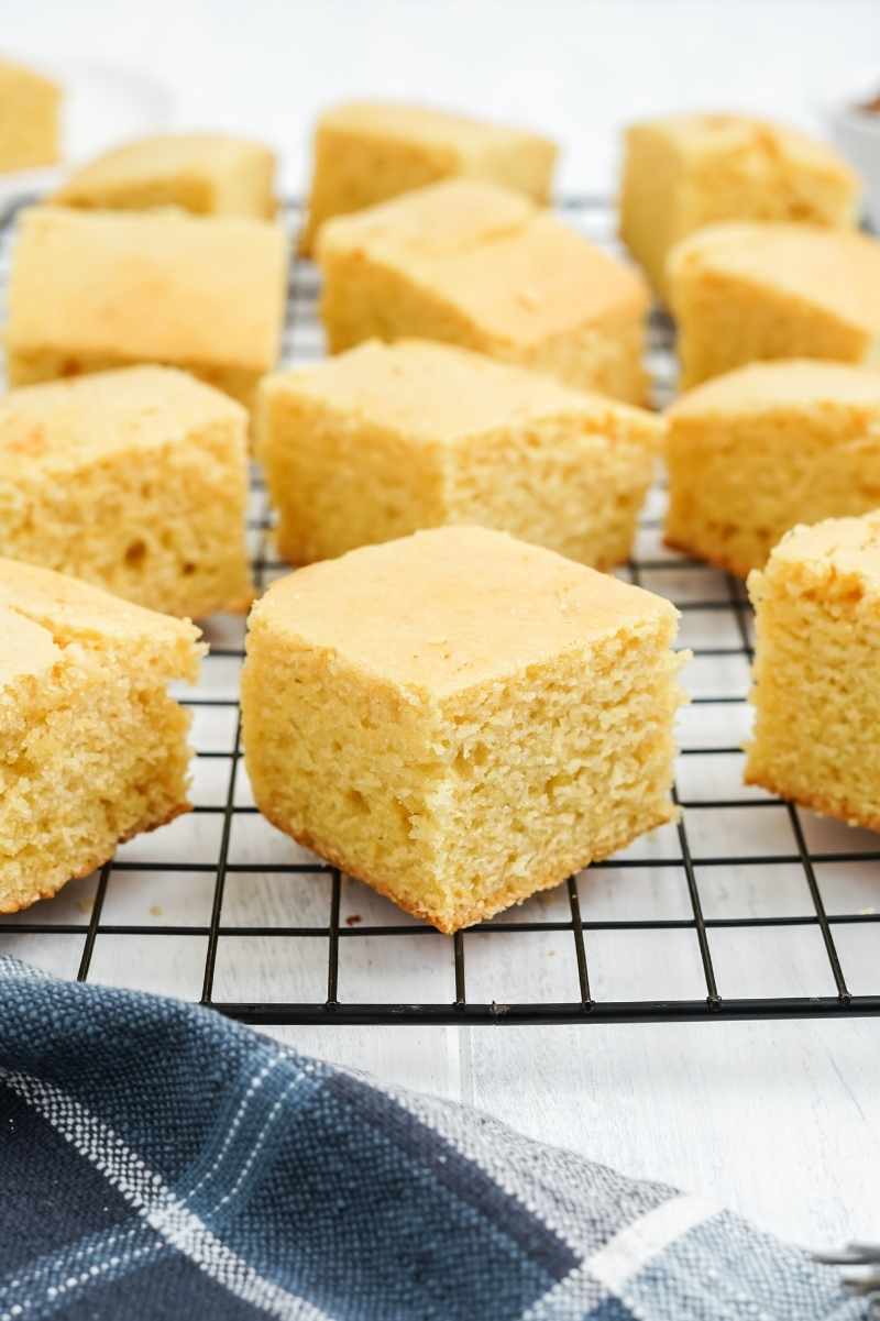 Tender squares of cornbread on a cooling rack with a blue and white kitchen linen nearby.