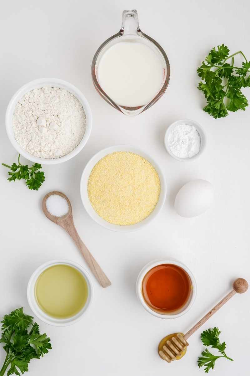 Overhead of ingredients used to make honey cornbread, including yellow cornmeal, flour, and buttermilk.