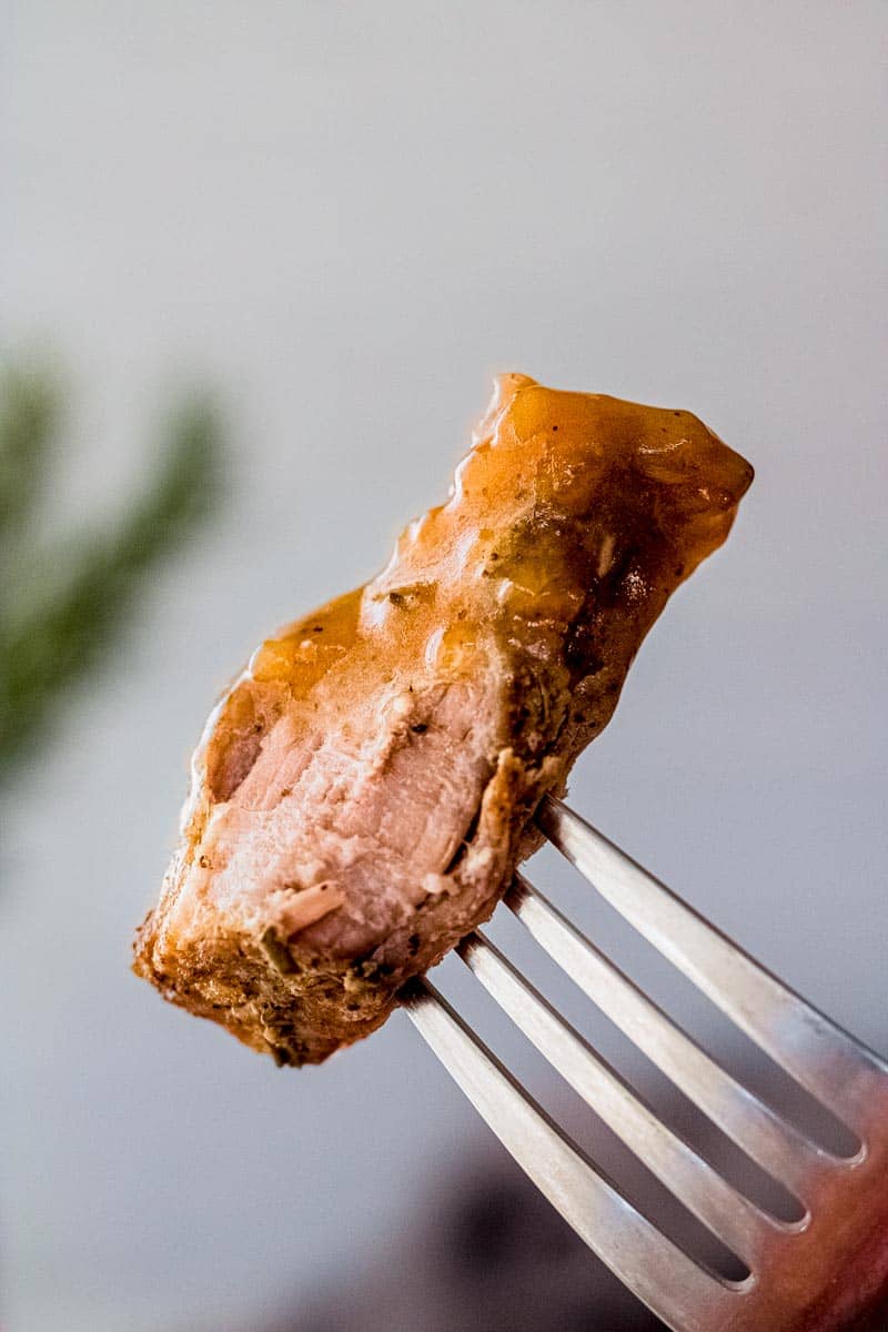 Close view of a piece of juicy pork roast topped with gravy on a fork.