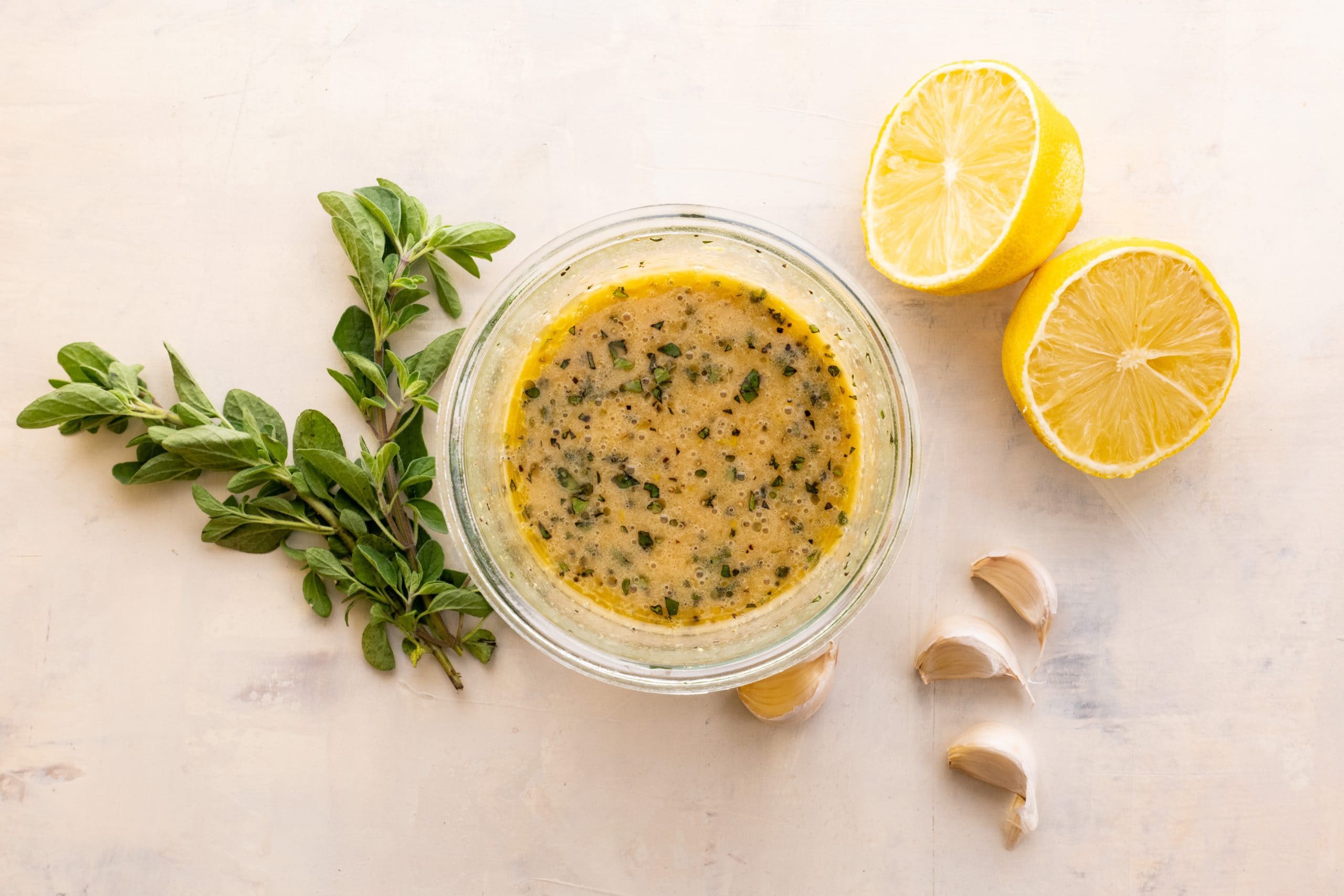 Birdseye view of simple lemon vinaigrette in a jar with fresh oregano, lemon, and garlic cloves around.