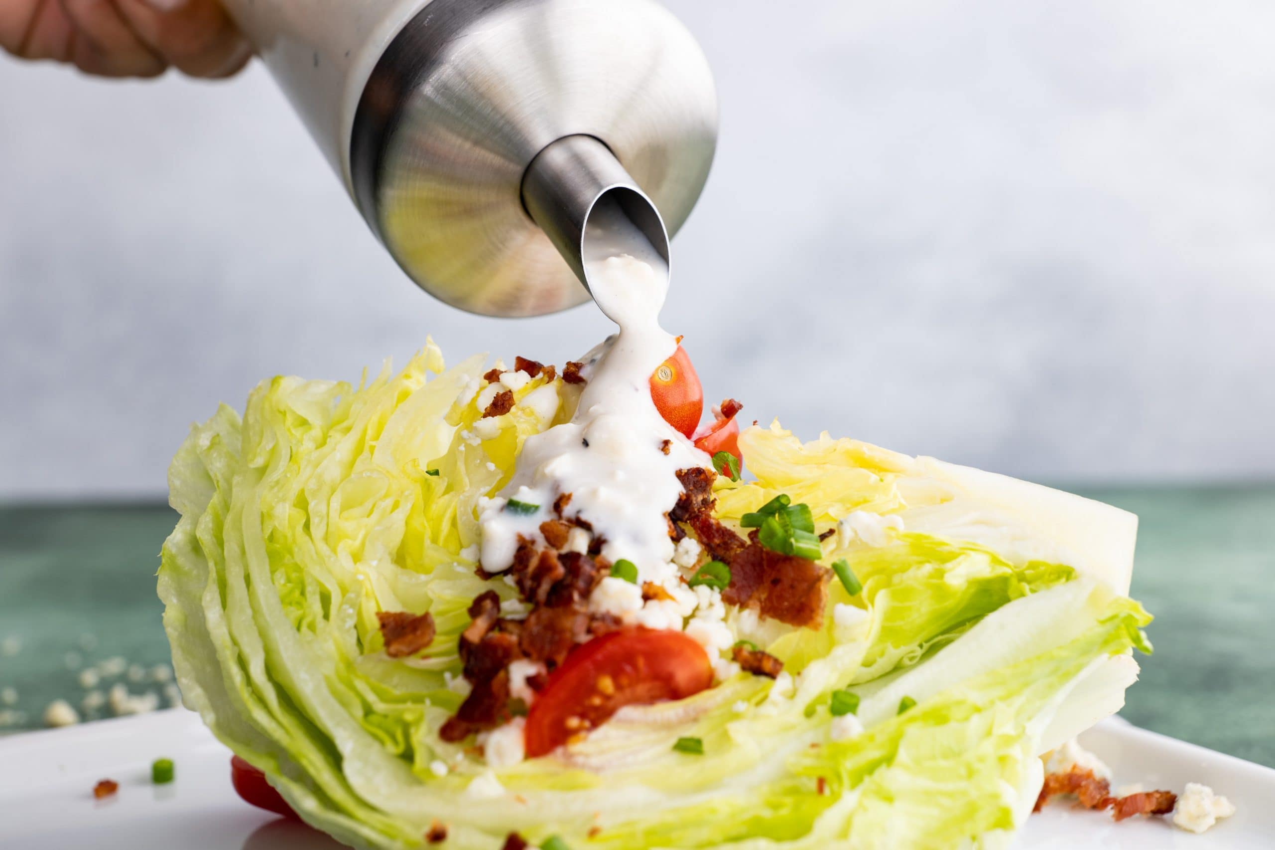 Close view of a hand pouring homemade dressing on an iceberg wedge salad.