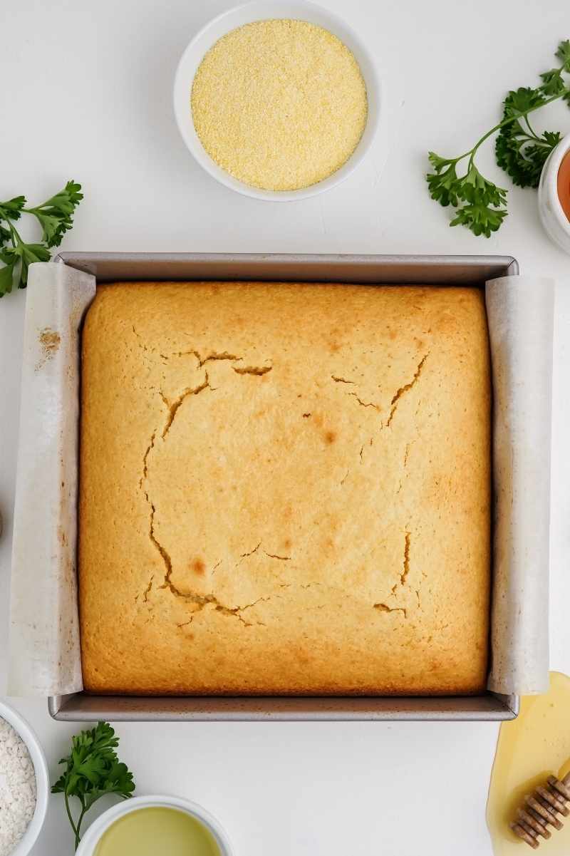 Top view of baked honey cornbread in a parchment lined square baking pan.