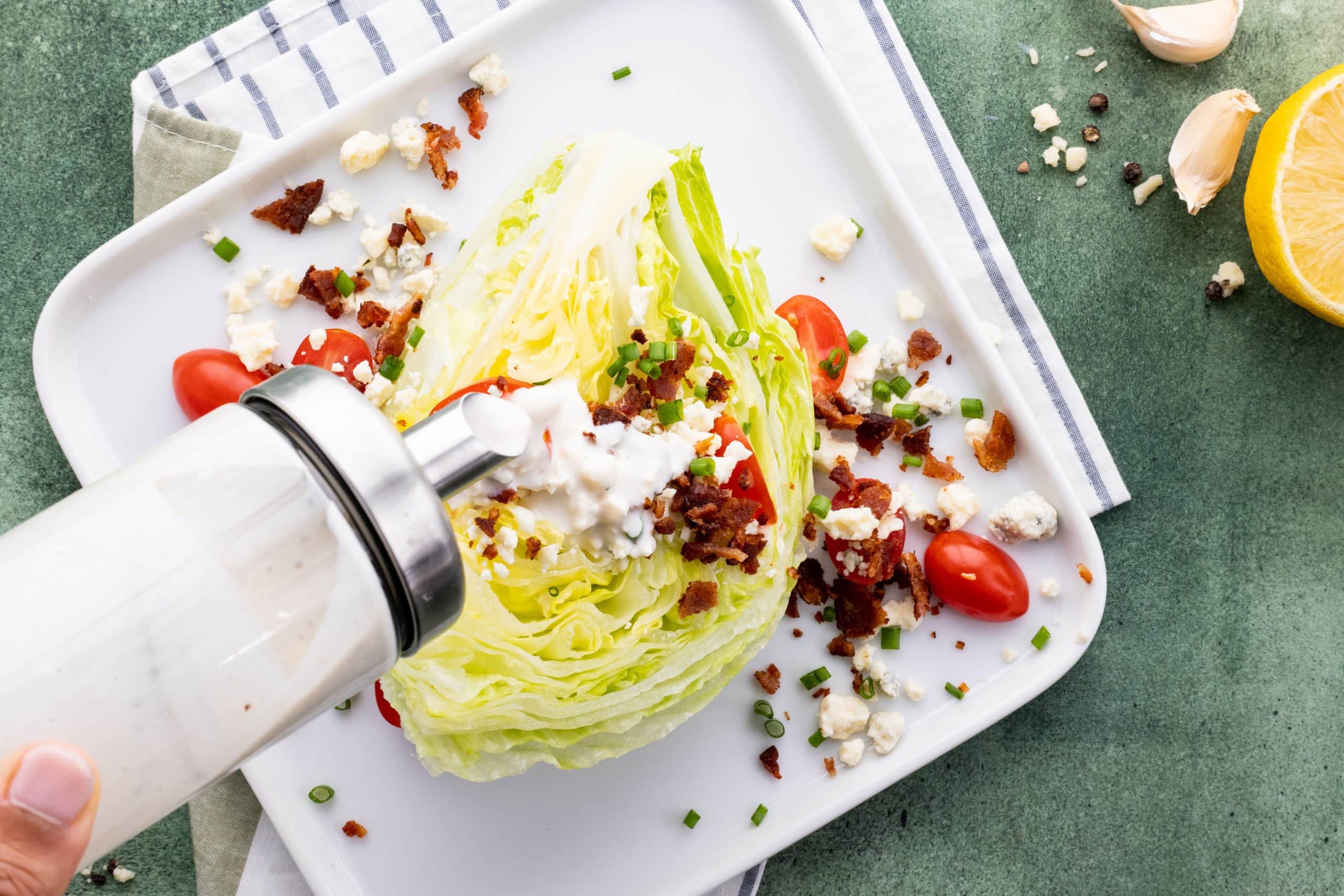 Overhead of a hand pouring blue cheese dressing onto an iceberg wedge salad.