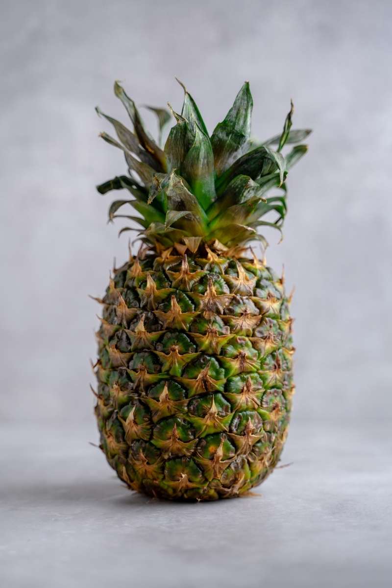 A whole pineapple stands uncut on a counter.