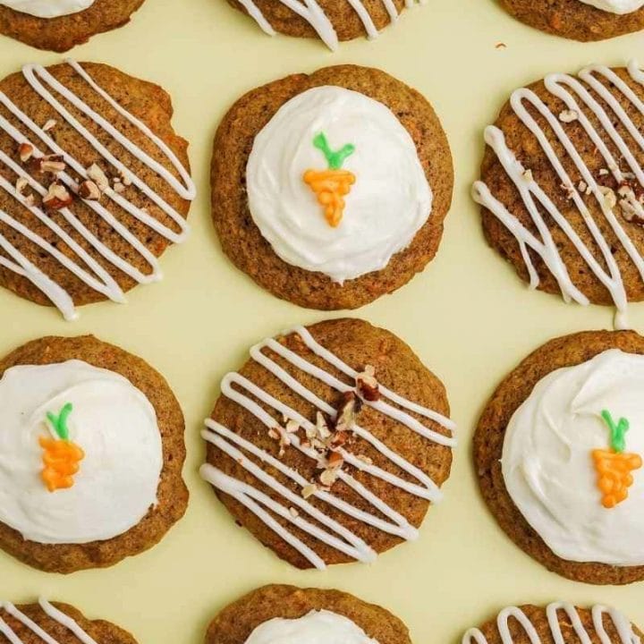 Alternating pattern of soft carrot cake cookies frosted two ways, half with full cream cheese frosting and a frosting carrot detail and half with a frosting drizzle and chopped nuts.
