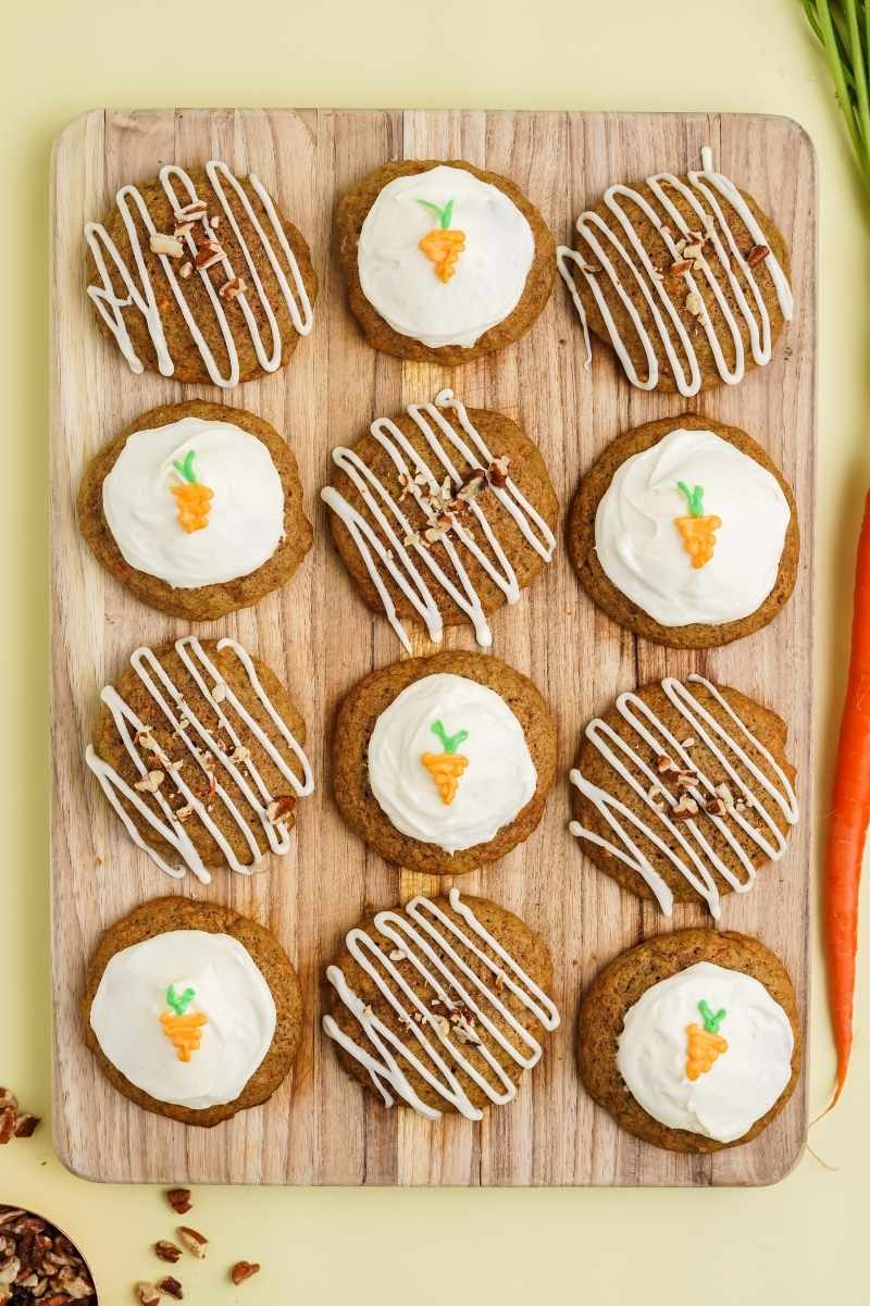 Birdseye view of frosted carrot cake cookies on a wooden cutting board.