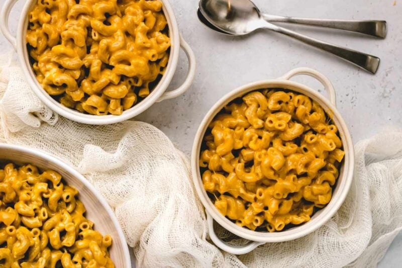Tight view of individual servings of instant pot mac and cheese in white bowls with spoons nearby.