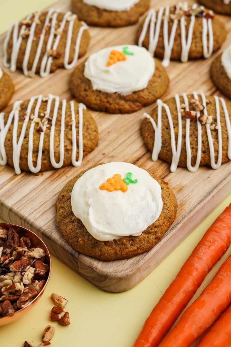 Close view of finished cookies on a cutting board with chopped nuts and carrots alongside.