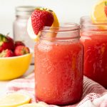 Close up on a jar full of a pink drink, garnished with fruit