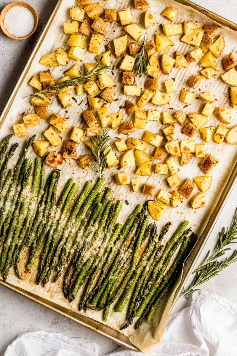 Birdseye view of a baking sheet with oven roasted potatoes and asparagus garnished with fresh rosemary.