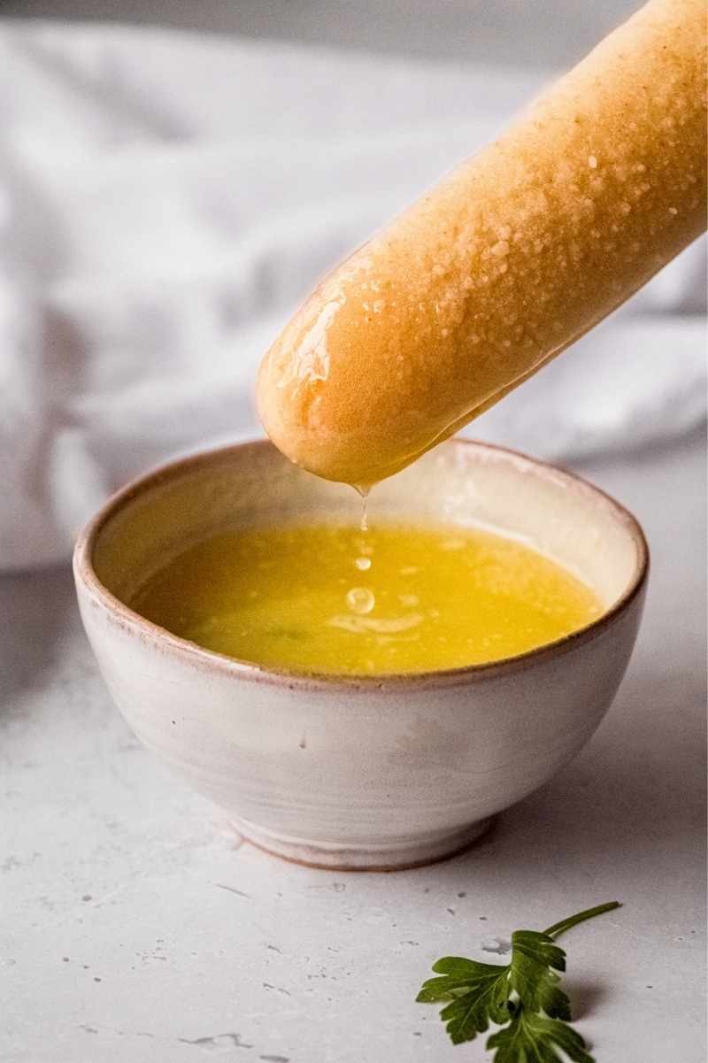 A soft breadstick dips into a bowl of melted garlic butter sauce.