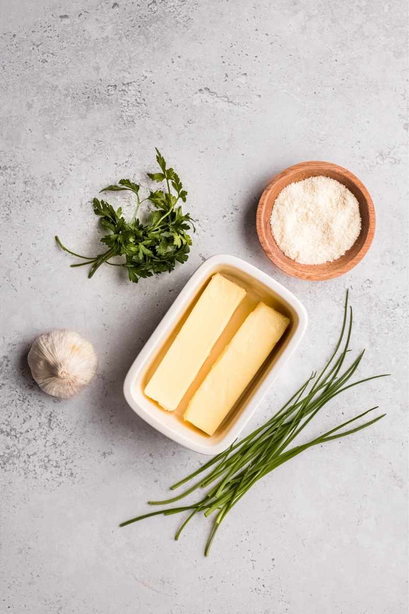 Five ingredients needed to make garlic butter including butter, herbs, garlic, and salt.