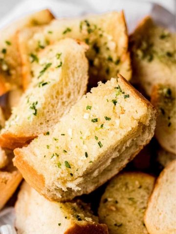 Close view of a pile of roasted garlic bread slices in a bread basket.