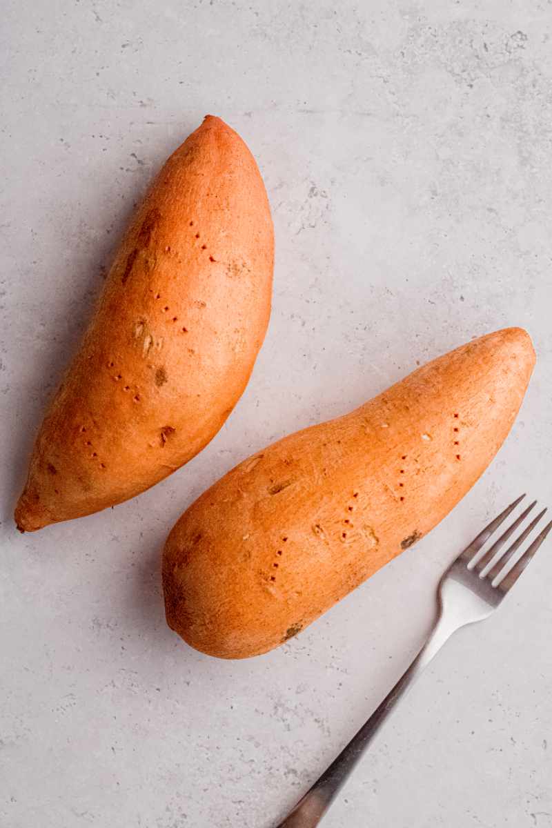Close view of two sweet potatoes with four pricks from a fork in each and a fork alongside.