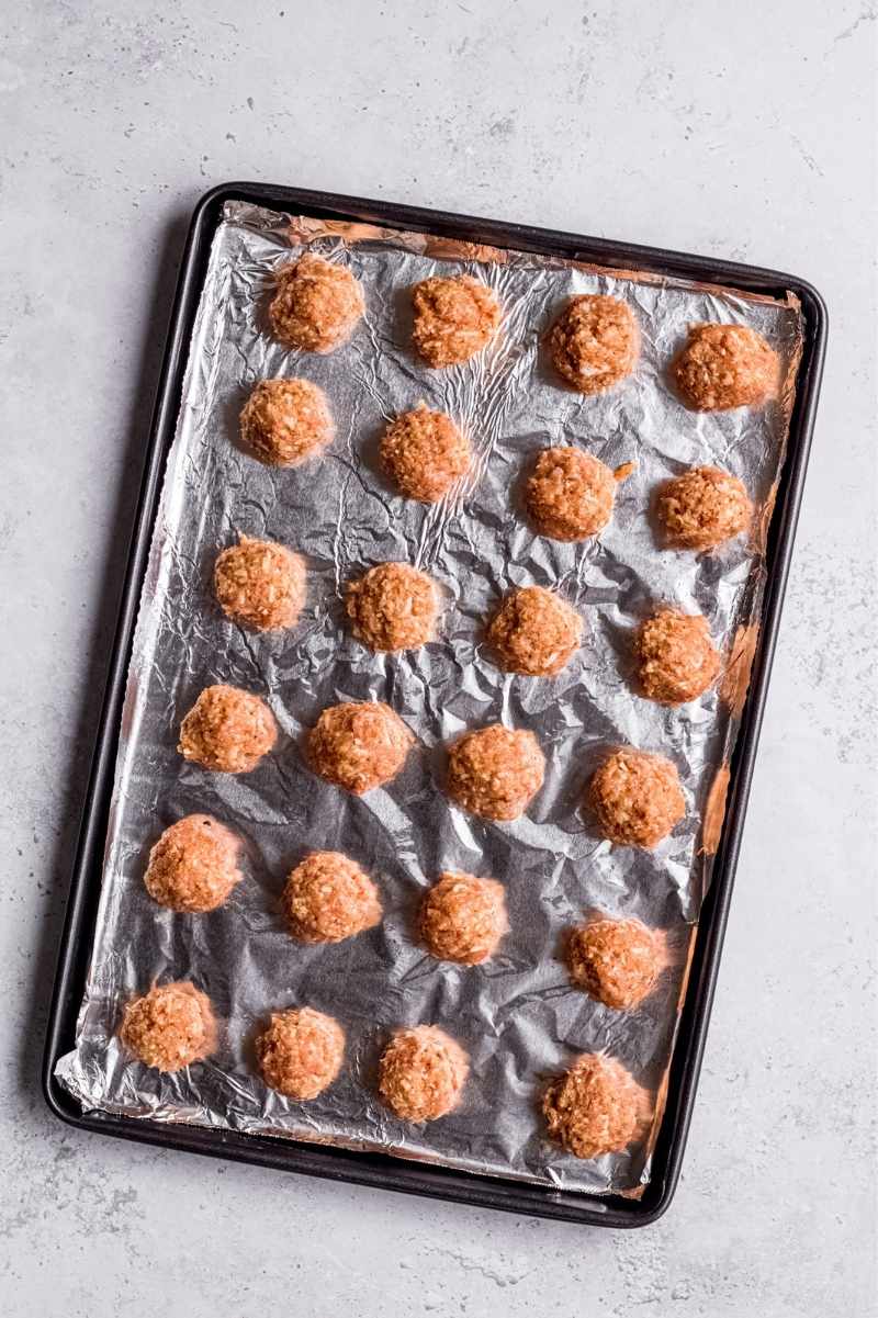 Rolled meatballs on a tinfoil lined sheet pan, ready to be baked.
