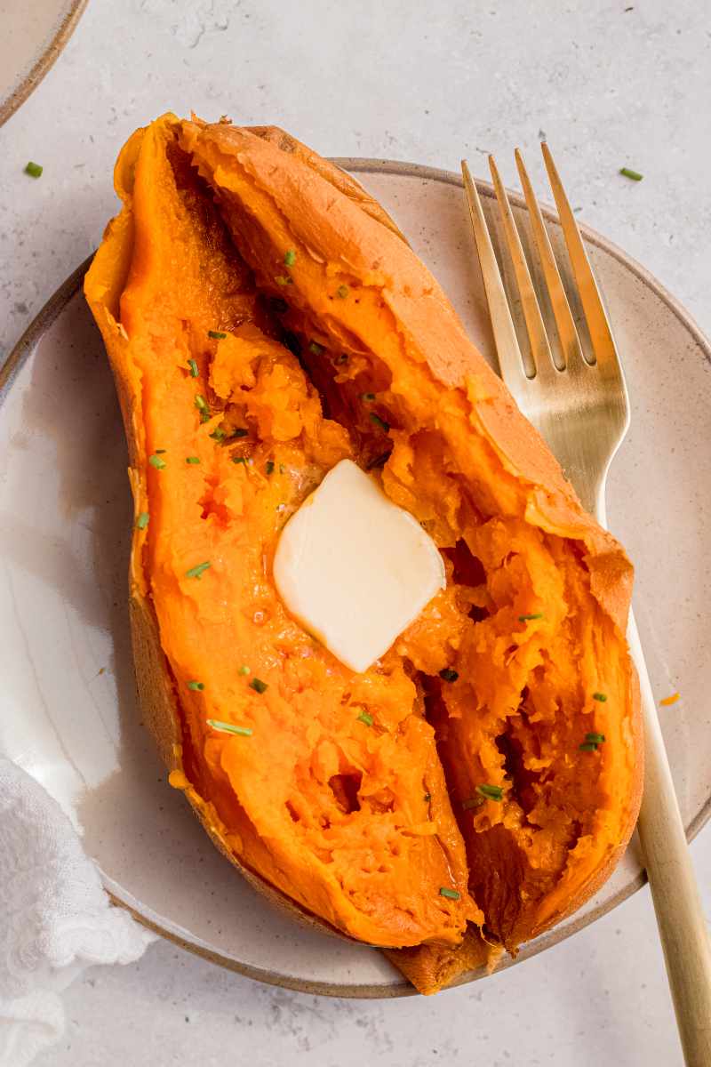 A baked sweet potato made in the instant pot served on a plate alongside a fork.