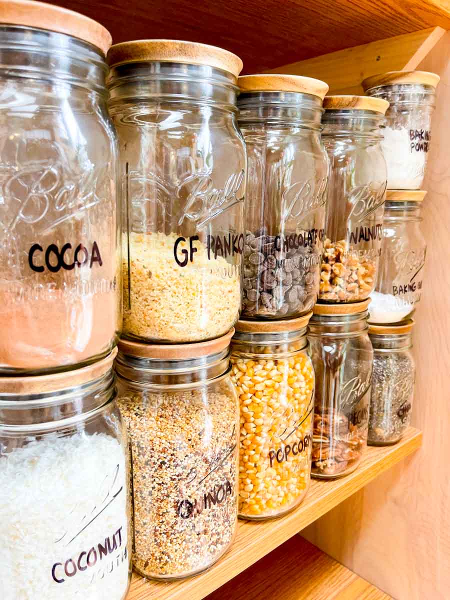 Side view of glass jars with airtight wooden lids filled with pantry essentials stacked on a shelf.