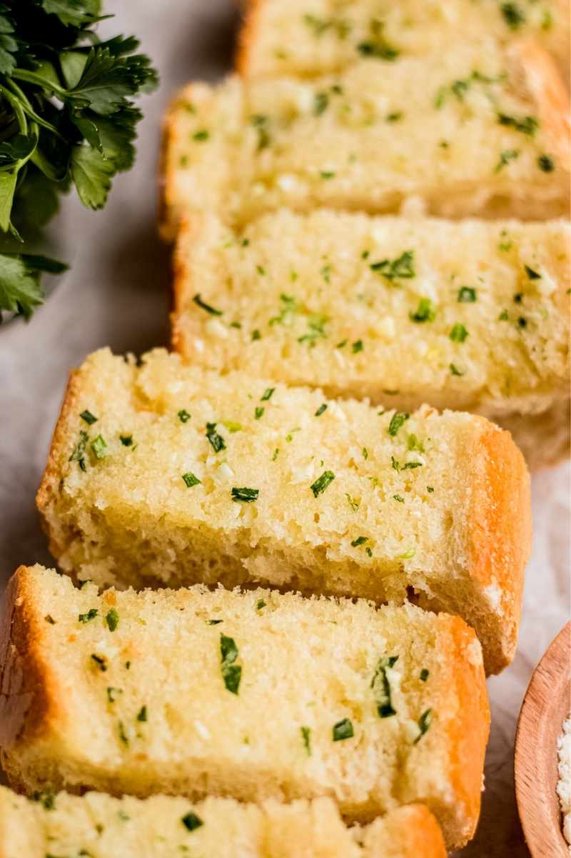 Close view of fluffy slices of buttery garlic bread flecked with minced fresh parsley.