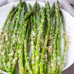 Finished oven roasted parmesan asparagus on a white serving platter with a fork nearby.
