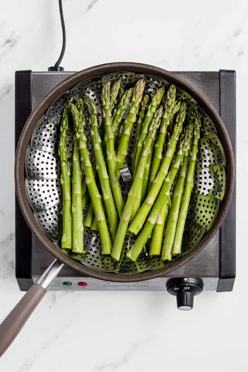Fresh asparagus spears in a steamer basket resting in a skillet.