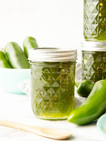 Fresh green jalapeno peppers and a wooden spoon rest beside a jar of pepper jelly.