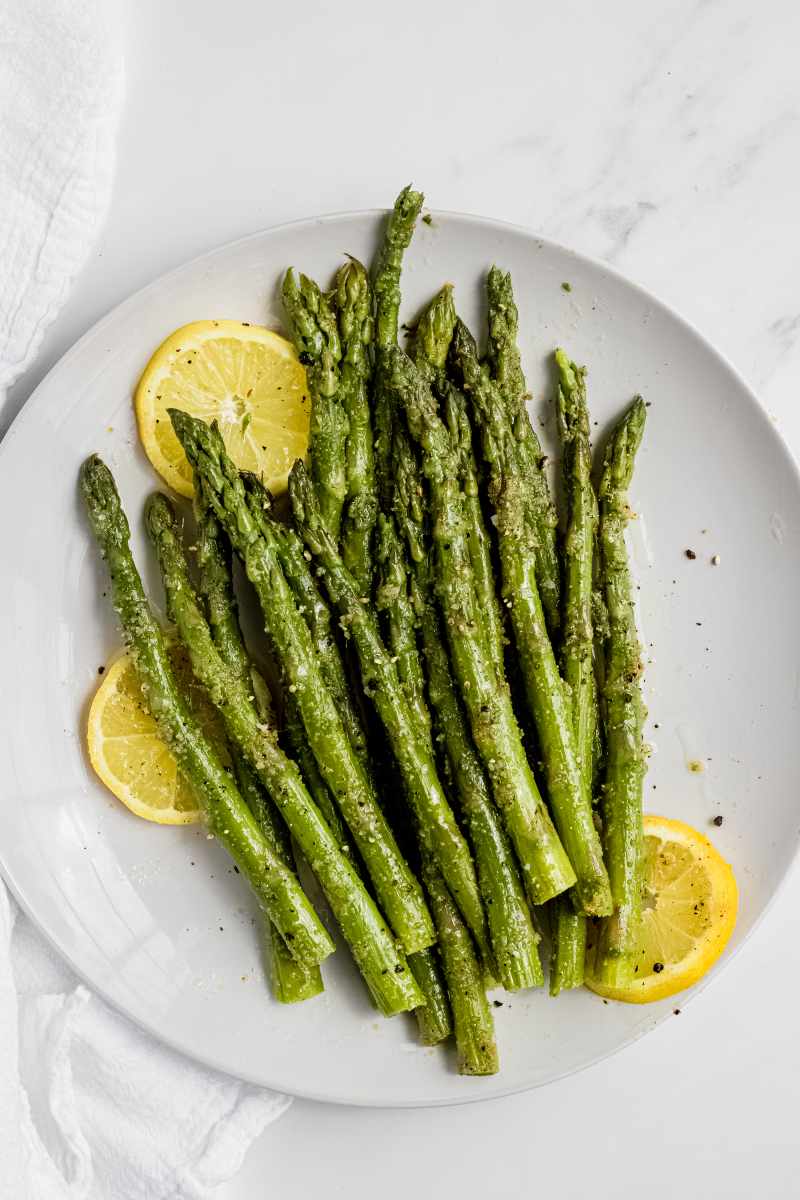 Seasoned, steamed asparagus on a round white plate with lemon slices.