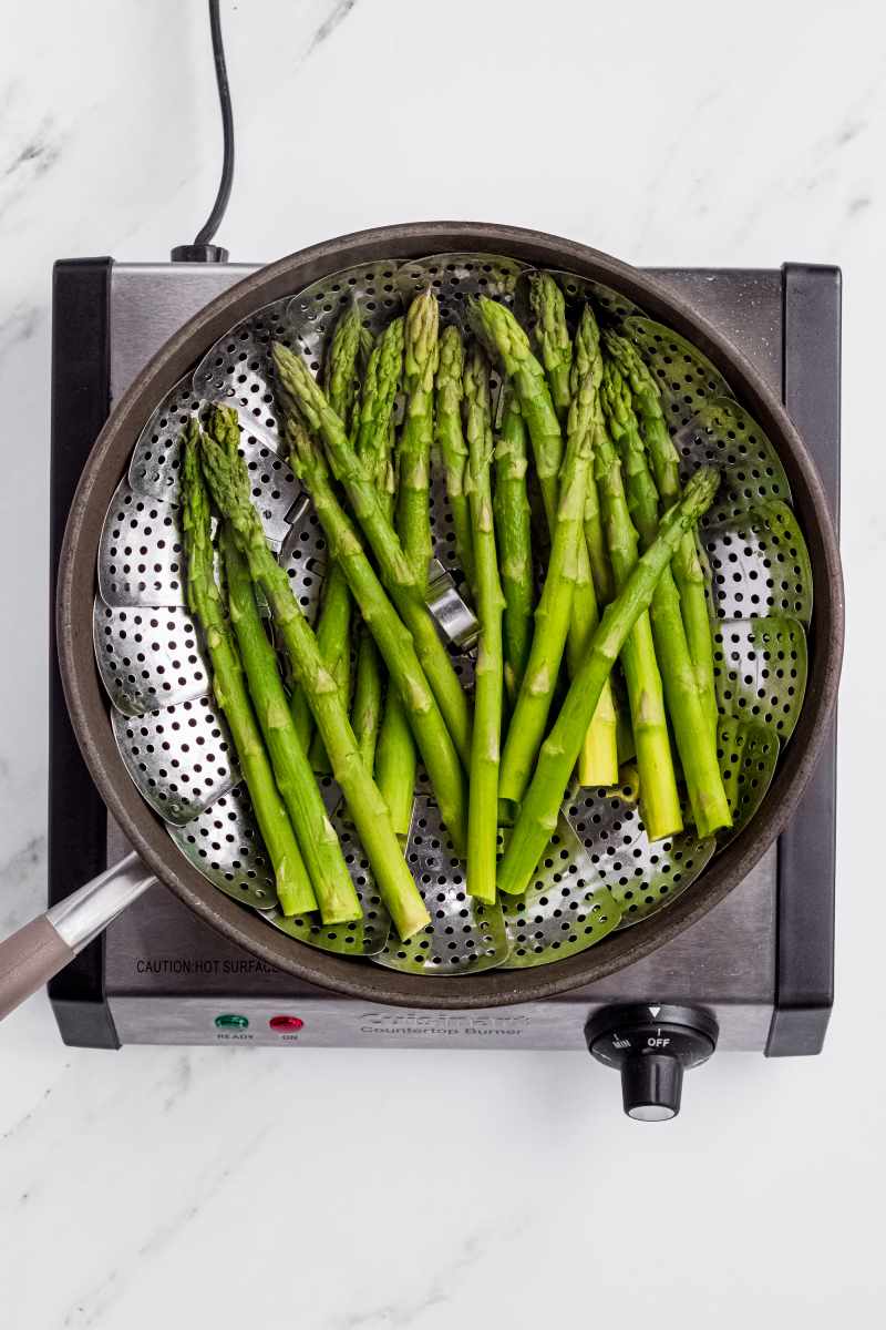 Green spears in a metal steamer basket after steaming.