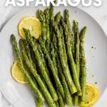 Seasoned, steamed asparagus on a round white plate with lemon slices. A text overlay reads, "Simple Steamed Asparagus."