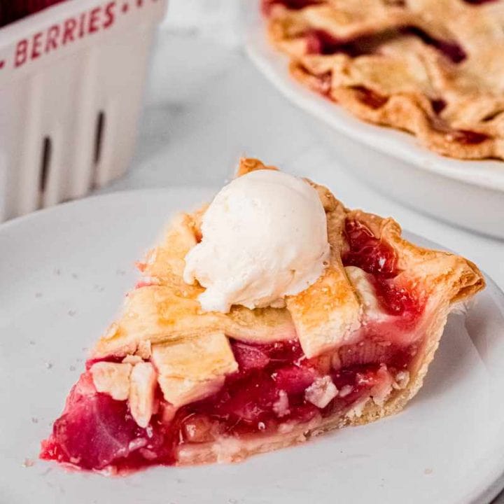 A single slice of strawberry rhubarb pie on a white plate topped with a small scoop of vanilla ice cream.