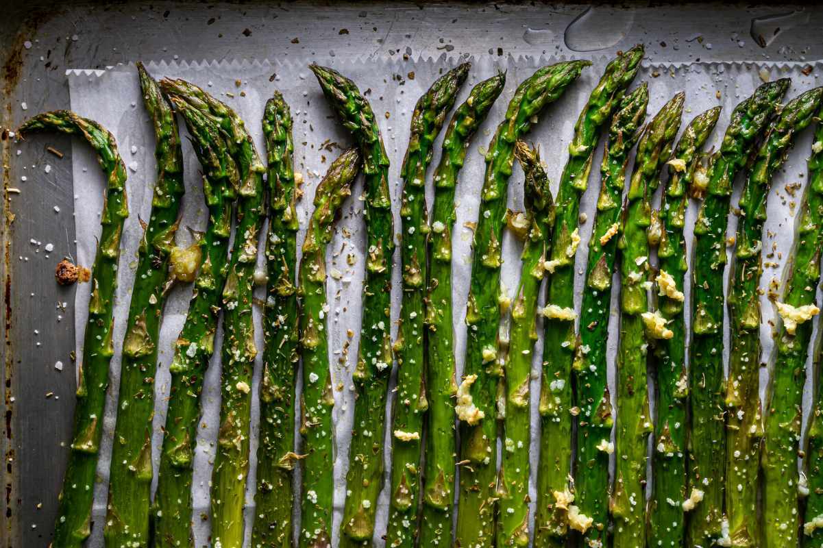 Close view of tender stalks of seasoned asparagus roasted on a parchment paper lined baking sheet.