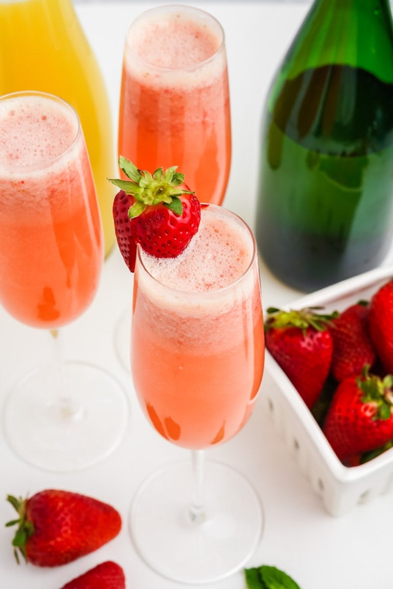 Top view of a frothy mimosa cocktail with a fresh strawberry garnishing the rim of the flute.