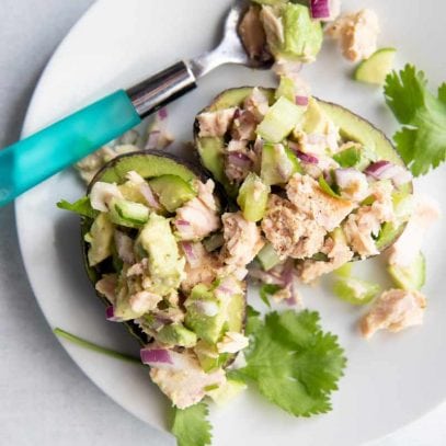 Birdseye view of a lunch serving of tuna salad with avocado, celery, cucumber, and red onion in two avocado halves.