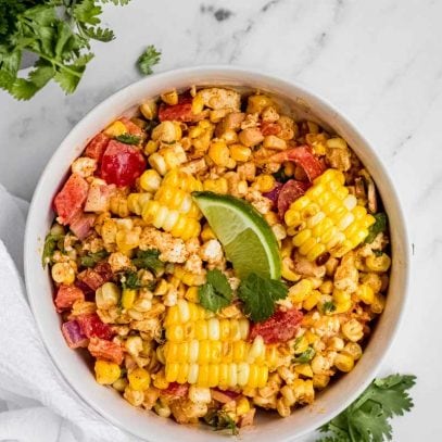 A serving bowl of finished mexican street corn salad garnished with cilantro leaves and a lime wedge.
