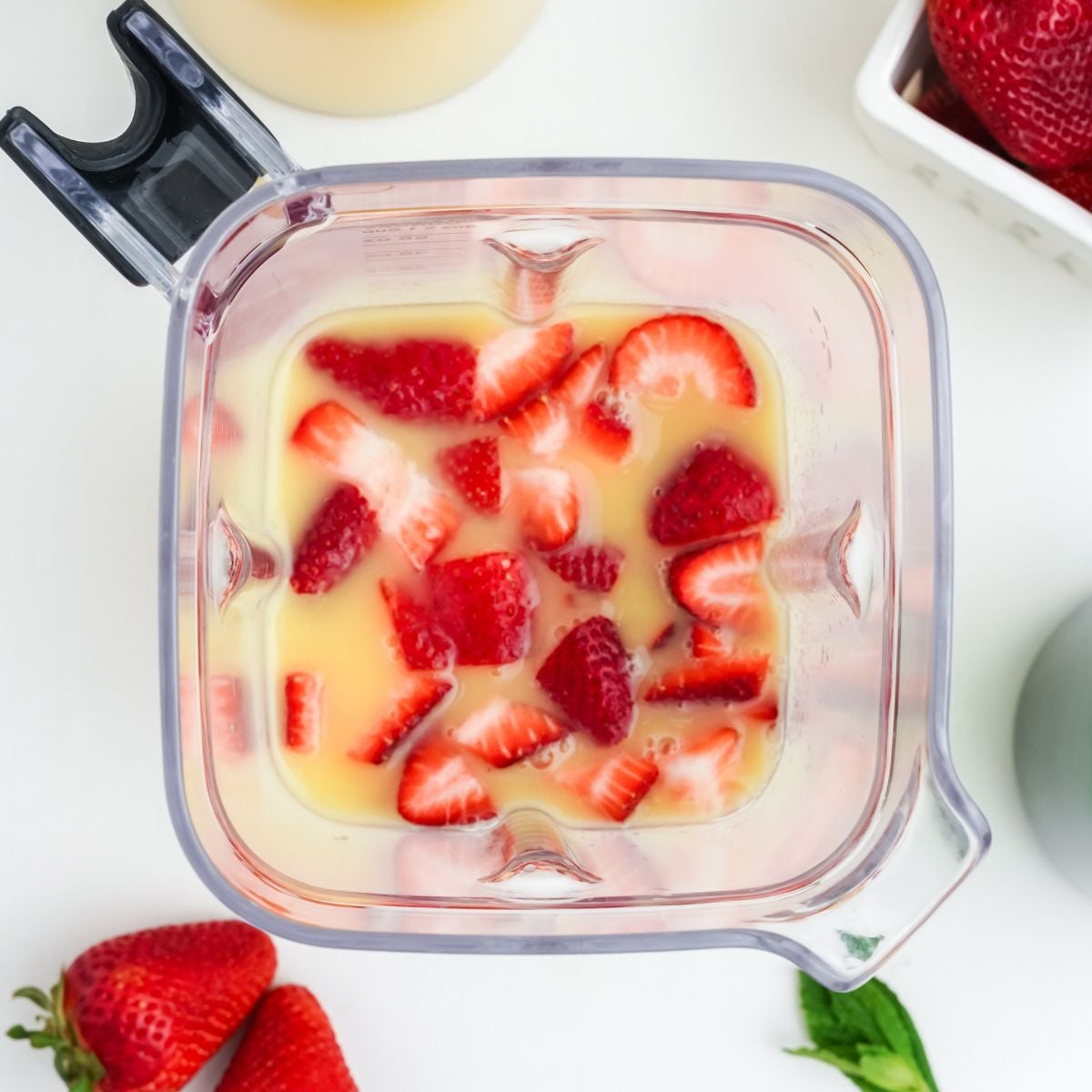 Blender filled with chopped strawberries and orange juice, with fresh strawberries on the counter