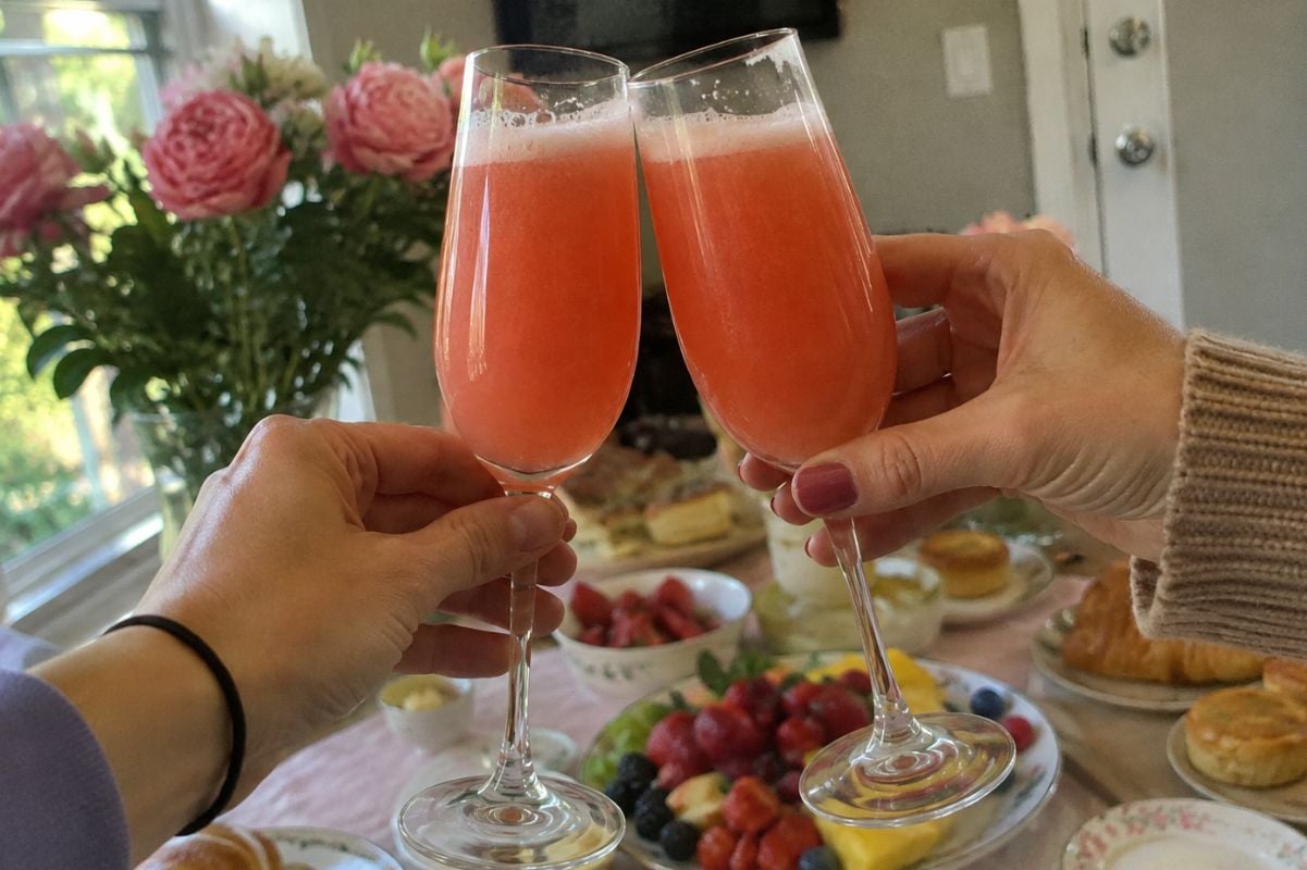 Two hands cheers strawberry mimosas in front of a Mother's Day breakfast