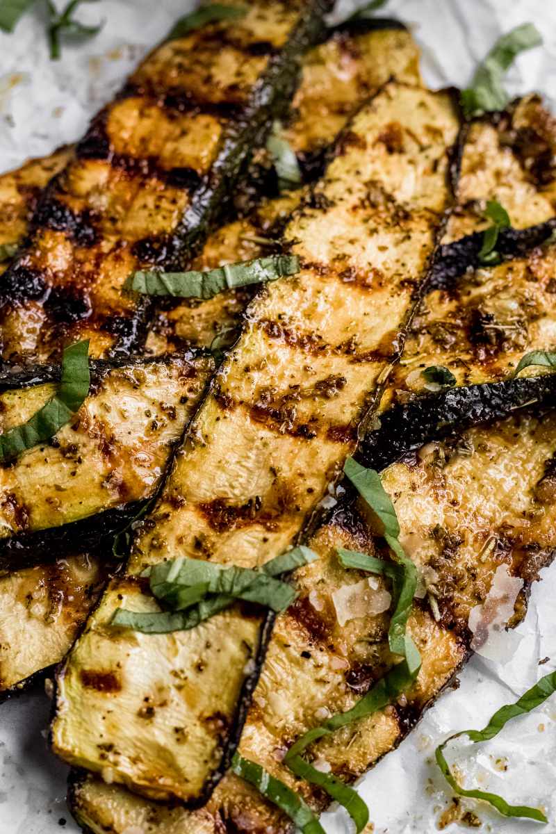Grilled parmesan zucchini slices piled on parchment paper garnished with ribbons of fresh basil.