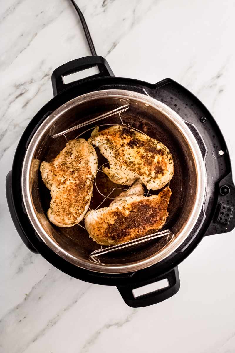 Three cooked chicken breasts on a trivet inside an instant pot.