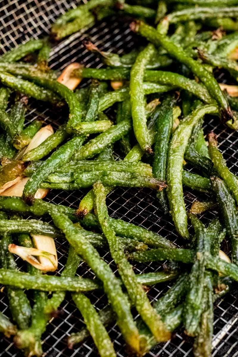 Tight view of cooking green beans in a grill basket on hot grill grates.