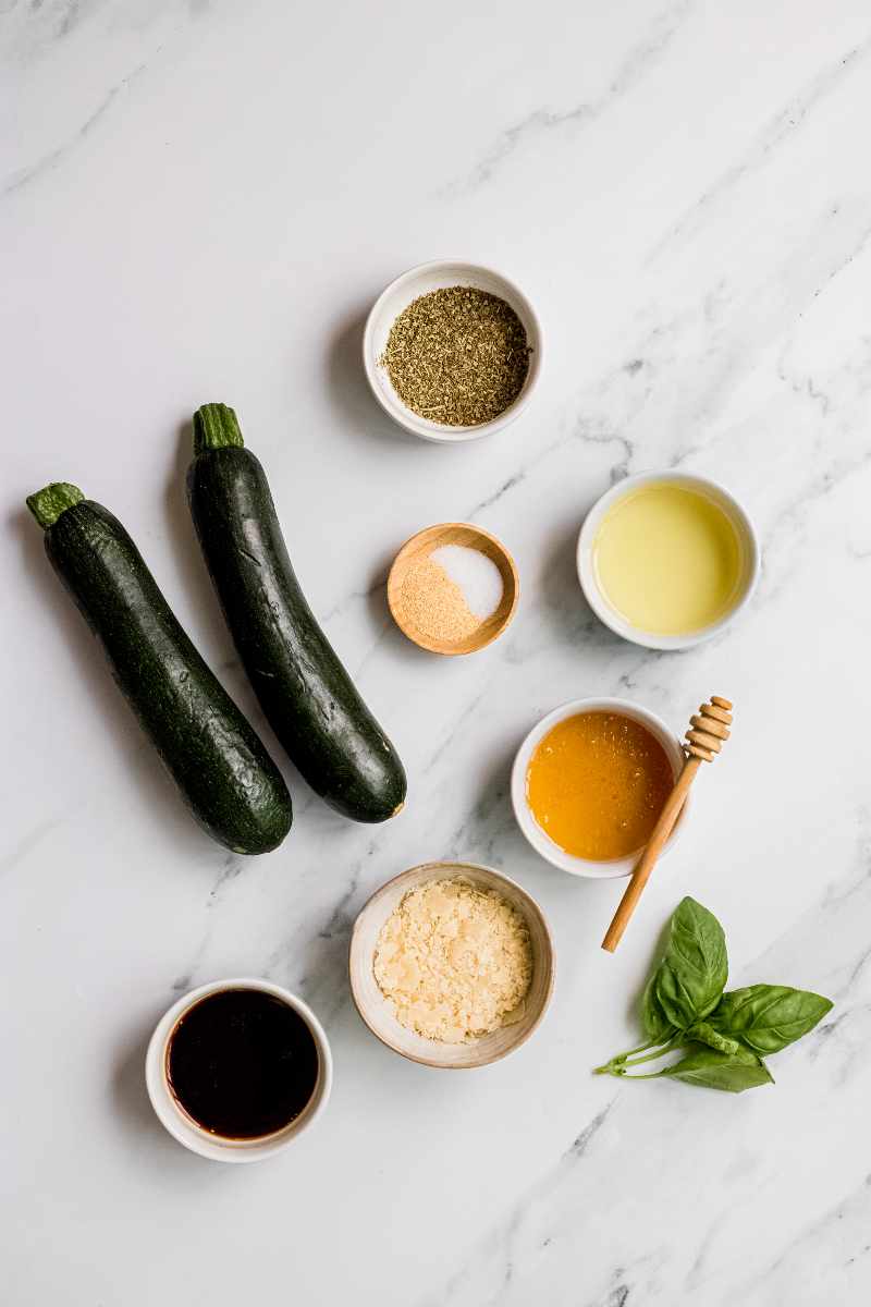 Overhead of ingredients needed to make grilled parmesan zucchini, including balsamic vinegar, prated parmesan, and garlic powder.