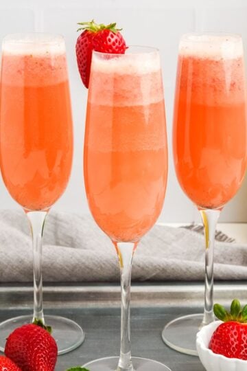 Square photo of three pink strawberry mimosas in champagne flutes