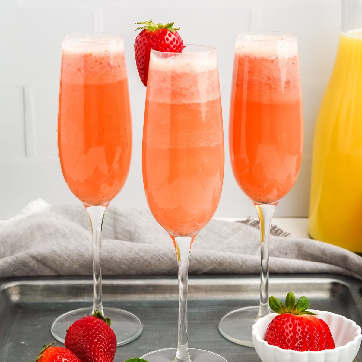 Square photo of three pink strawberry mimosas in champagne flutes