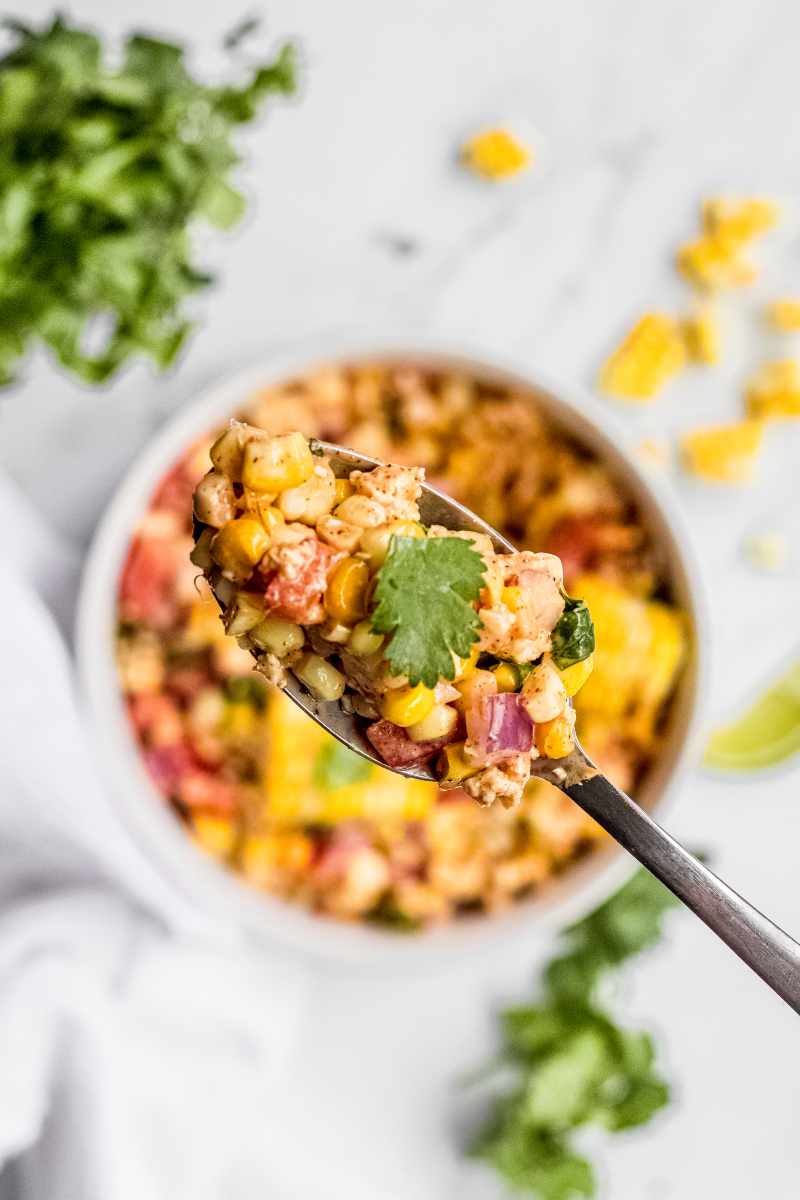 Close view of a full spoon of corn salad held above a serving bowl of salad in the background.
